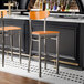 A bar stool with a cherry wood seat and back, and a metal frame with a clear coat finish.