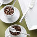 A Oneida Libra stainless steel teaspoon in a cup of coffee beans on a table.