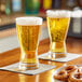 Two Libbey pilsner glasses of beer on a table.