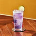 An Arcoroc Stack Up beverage glass filled with purple liquid and a lime wedge on a coaster.