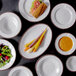 A white bowl of soup on a table with other white bowls and plates.