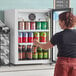 A woman opening an Avantco countertop display refrigerator with a beverage inside.