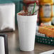 A Dart white foam cup with a lid on a table next to a sandwich.