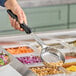 A person using a Vollrath black perforated Spoodle over a bowl of salad.