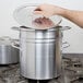 A hand opening a lid to a large silver pot using a black knob.