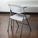 A white Lancaster Table & Seating plastic folding table with a white plastic chair sitting on top.