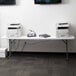 A Lancaster Table & Seating granite white folding table with white folding chairs set up in a room with a printer and books on it.