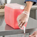 A person pouring pink liquid into a Lavex plastic container.