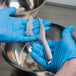 A person in blue gloves using a Winco shrimp deveiner to remove the shell from a piece of shrimp in a bowl.