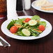 A Diamond White melamine bowl filled with a salad with tomatoes, cucumbers, and carrots.
