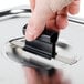 A hand holding a black Vollrath Kool Touch clip over a stainless steel pan.