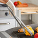 A person using Edlund heavy-duty gripper tongs to grill corn on the cob.