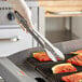 A person in gloves using Edlund heavy-duty scallop tongs to grill food.