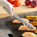 A person using Edlund Heavy-Duty Scallop Utility Tongs to grill food.