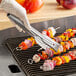 A person holding Edlund heavy-duty gripper tongs over food on a grill.