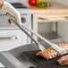 A person using Edlund heavy-duty tongs to grill meat.