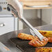 A person using Edlund heavy-duty tongs to grill food.