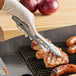 A person using Edlund Heavy-Duty Scallop Utility Tongs to cook meat on a grill.