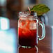 An Arcoroc mason jar with a drink and ice on a table with a leaf on top.