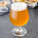 A glass of Arcoroc Belgian beer with foam next to a bowl of nuts.