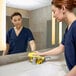 A yellow 12-inch by 12-inch recycled microfiber cleaning cloth being used to wipe a bathroom sink area.