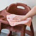 A hand using a pink Rubbermaid HYGEN microfiber cloth to clean a chair