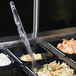 A clear plastic Cambro salad bar spoon in a tray of food.