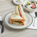 A Tuxton Green Bay Ivory china plate with a sandwich and fruit.