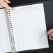 A person using a blue pen to write on Menu Solutions reservation book pages.