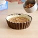 A person pouring pecans into a small fluted tart pan.