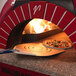 A GI Metal square perforated pizza peel with a pizza in a wood oven.