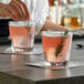 A person pouring a pink drink into an Anchor Hocking New Orleans Old Fashioned glass on a table.