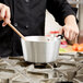 A person using a Vollrath Wear-Ever sauce pan with a black silicone handle to cook on a stove.