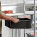 A black polyethylene bus tub with a ribbed bottom being held by a person in a commercial kitchen setting.