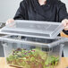 A woman holding a Carlisle clear plastic food storage container with a lid full of salad.