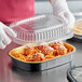 A gloved hand holds a black and gold Durable Packaging foil container of food.