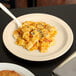 A close-up of a Cambro beige polycarbonate plate of pasta with a spoon.