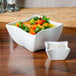 A bowl of salad with vegetables and a white bowl of sauce on a table.