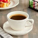 An Acopa Ivory stoneware coffee cup on a saucer with a cup of coffee on a table with pastries.