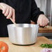 A person stirring food in a Vollrath aluminum sauce pan.