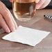 A hand holding a glass of white liquid over a white 2-ply napkin.