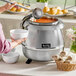 A woman using an Avantco stainless steel soup kettle to fill a white bowl with soup.