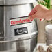 A person using an Avantco stainless steel soup kettle to serve clam chowder on a hotel buffet counter.