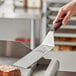 A hand using a Mercer Culinary Hell's Handle turner to cut a steak.