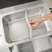 A hand using a Vollrath adapter bar to hold stainless steel containers over a sink.