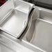 A Vollrath stainless steel adapter bar in a stainless steel sink with two food containers.