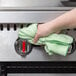 A hand holding a green Rubbermaid microfiber cloth wiping a kitchen surface.