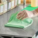 A green recycled microfiber cloth being used to clean a surface.