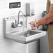 A man washing his hands in a wall mounted Regency hand sink under a faucet.