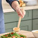 A person using a Cambro beige plastic ladle to scoop sauce onto a plate of vegetables.